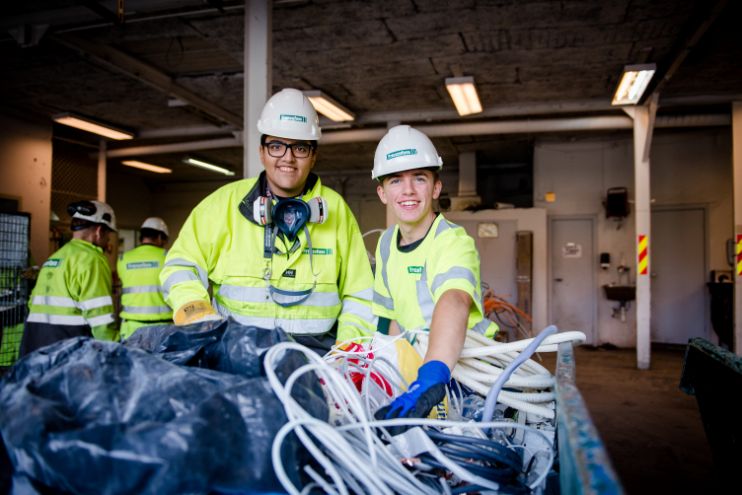 To menn ikledd arbeidsantrekk og hjelm håndterer avfall
